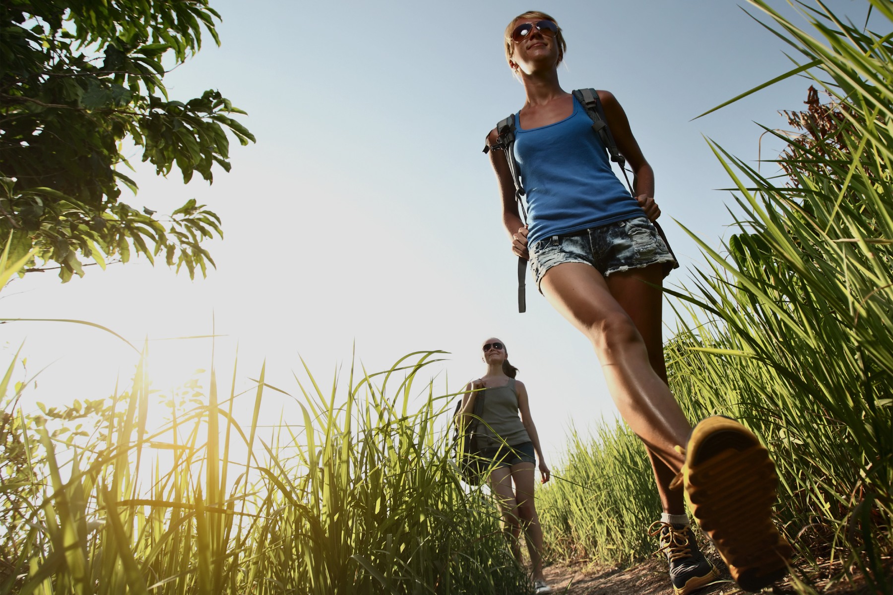 Fotografía de dos mujeres andando por el monte entre hierba y con mochilas