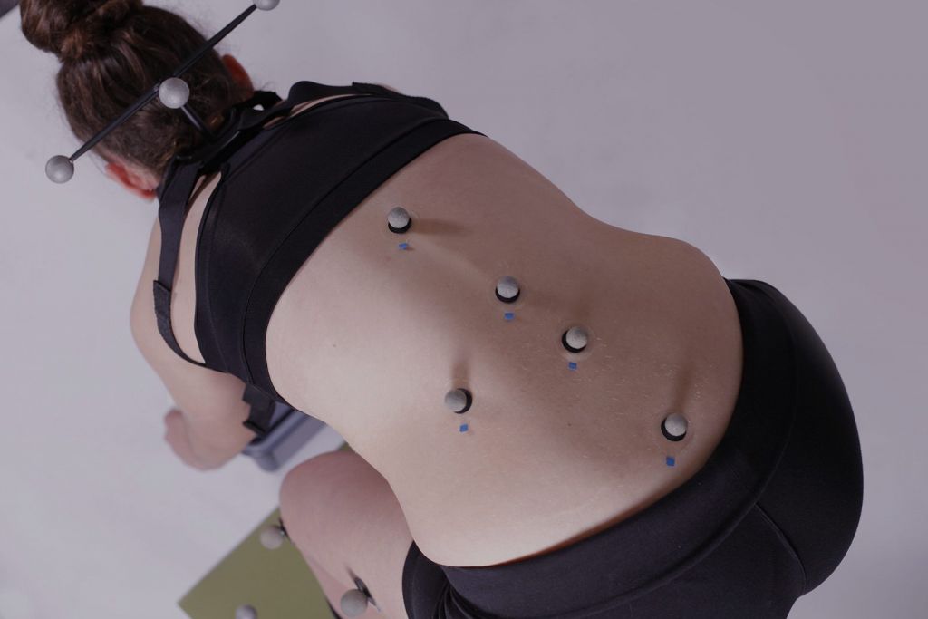 Fotografía de una mujer agachada con electrodos en la espalda para una prueba