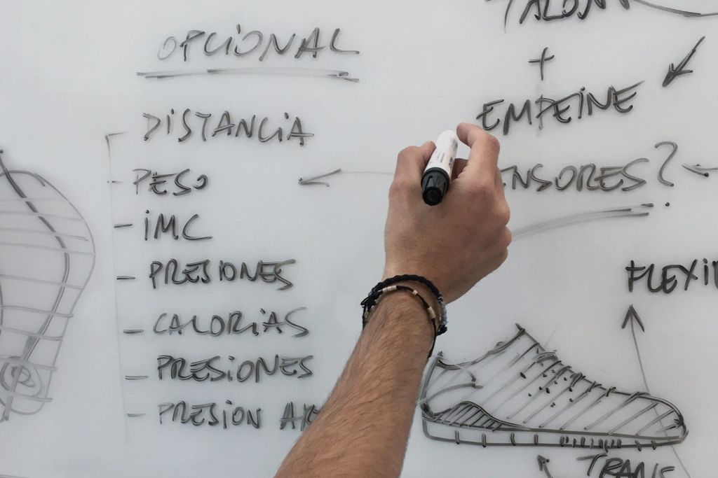Fotografía de técnico escribiendo en pizarra la descripción del prototipo de una zapatilla deportiva