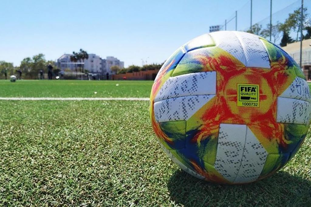 Fotografía de una pelota de fútbol con el logotipo de la FIFA en un campo de fútbol de césped artificial