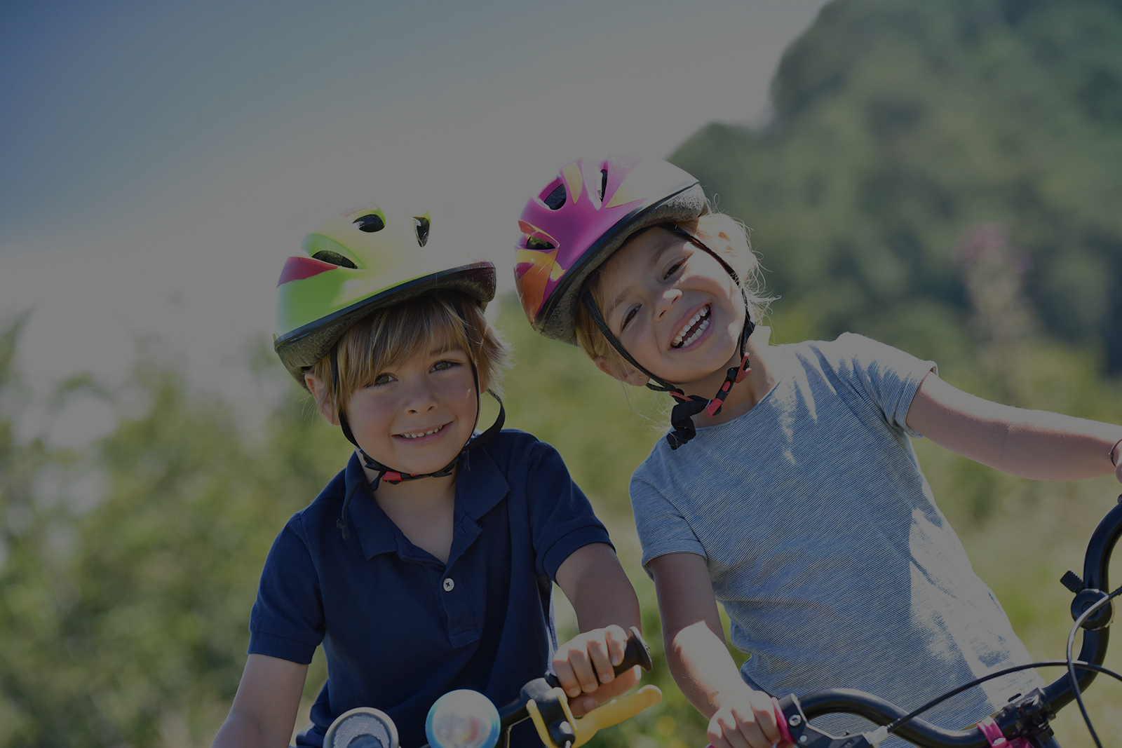 Fotografía de un niño y una niña con cascos de bicicleta sonriendo a la cámara